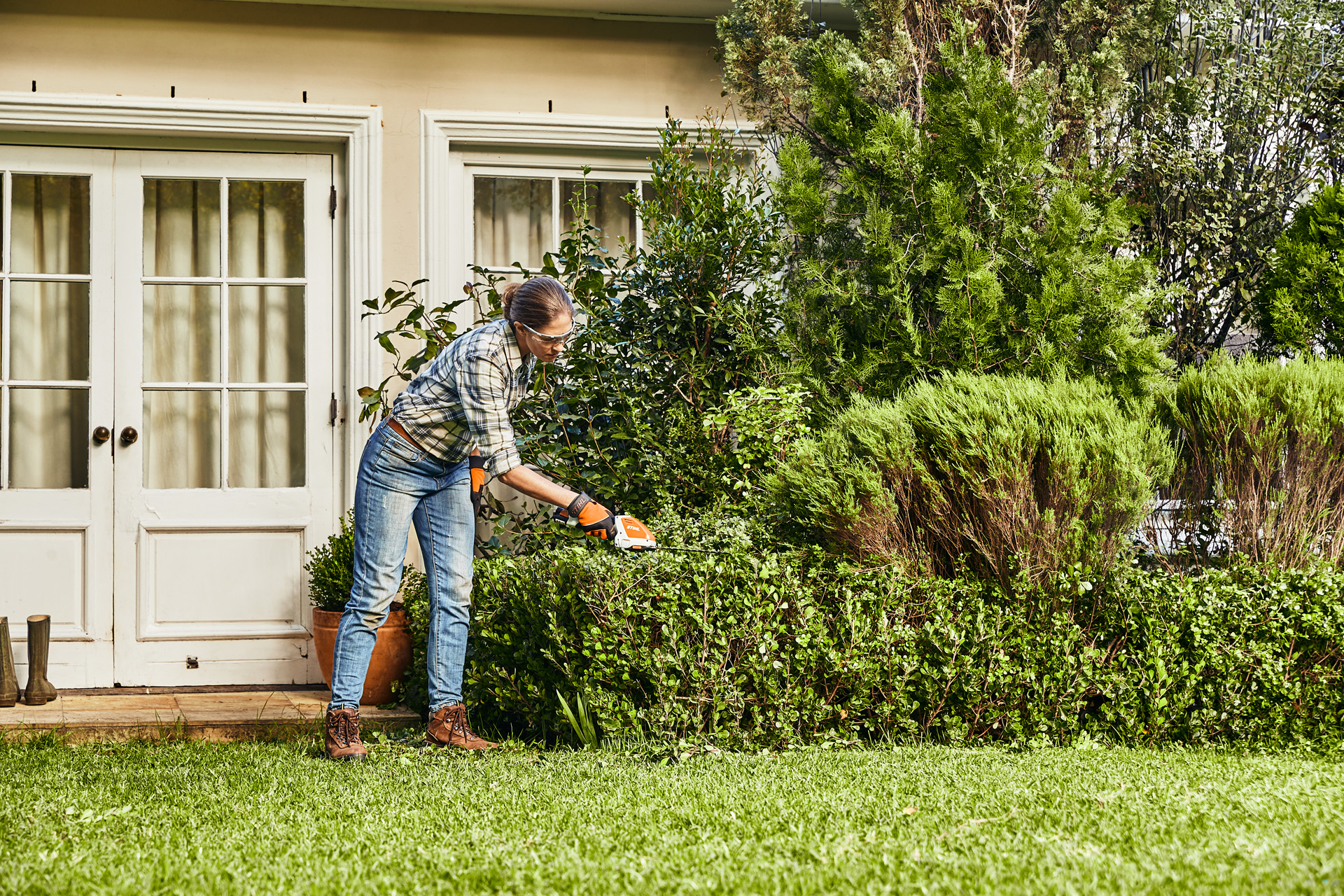 Woman trimming a box hedge in front of a white house using a STIHL HSA 26 cordless hedge trimmer