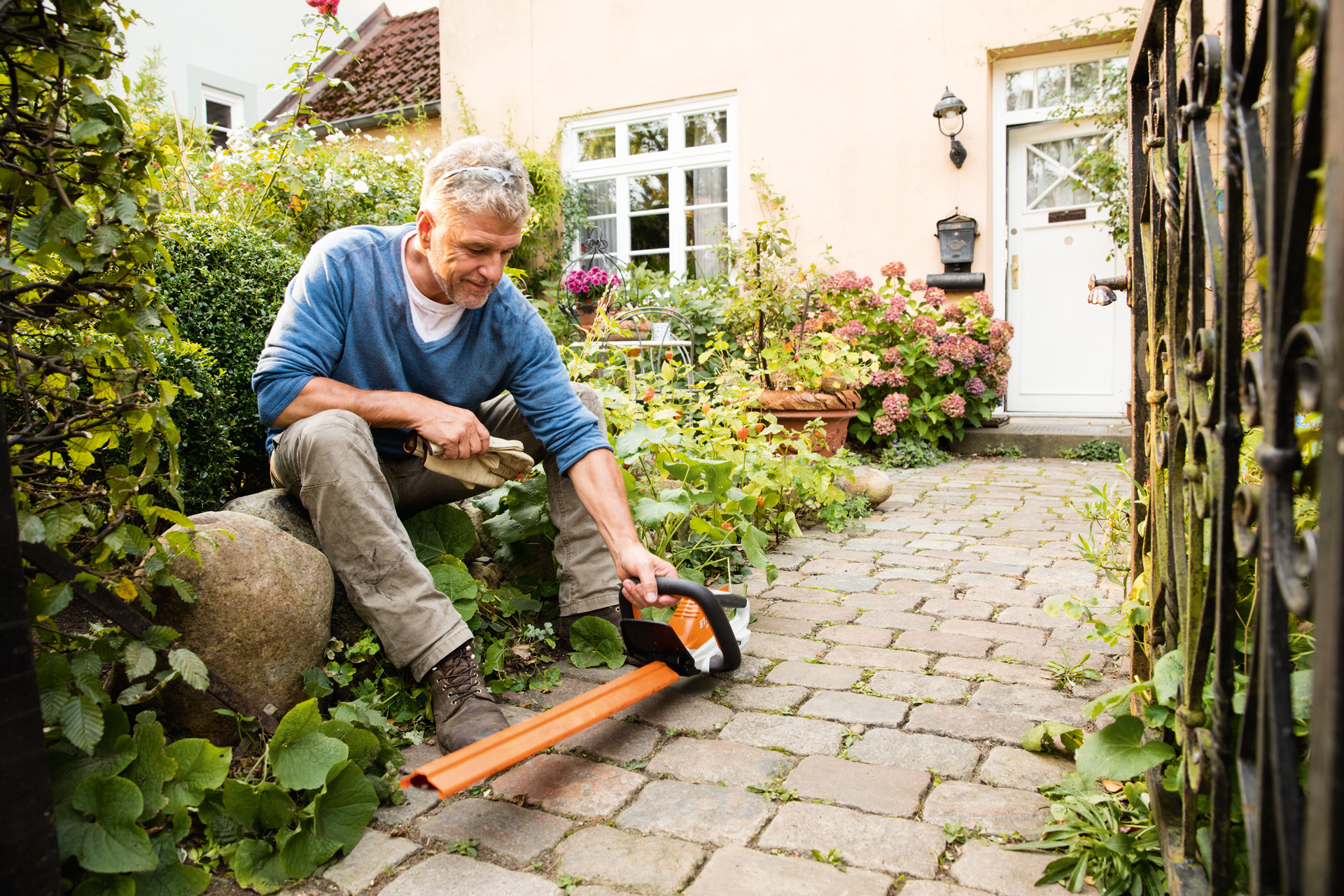 A man with an AI Series STIHL HSA 45 electric hedge trimmer in front of a house