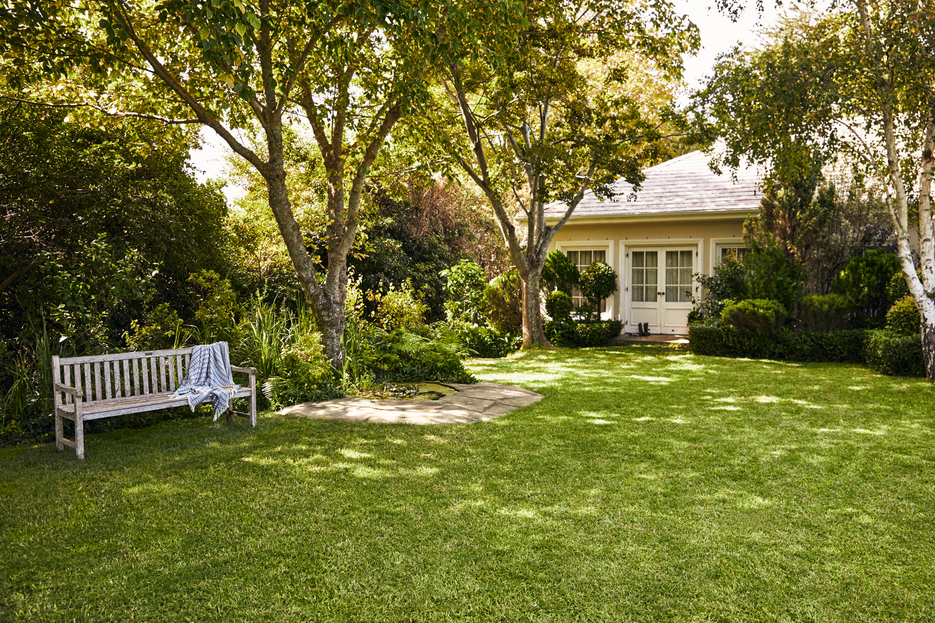 Small house with garden; in the foreground, a garden bench on a green lawn